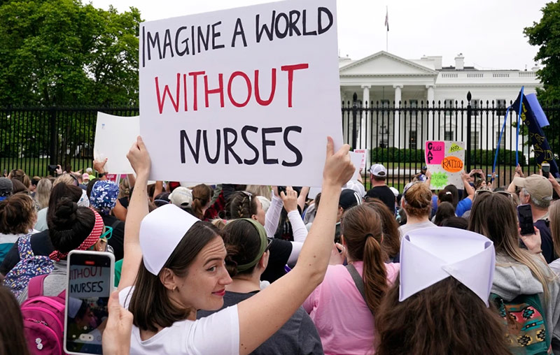 Individual dressed in nurse uniform holds a protest sign in front of the White House stating 'Imagine a World without Nurses'